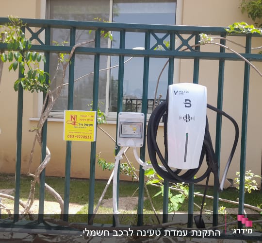 מטען חשמלי לרכב תלוי על גדר עם כבל